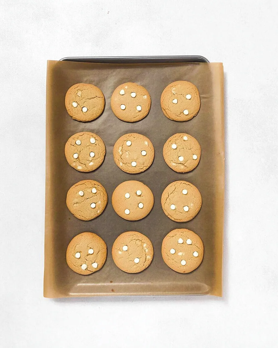 Baked white chocolate chip cookies on a baking sheet.