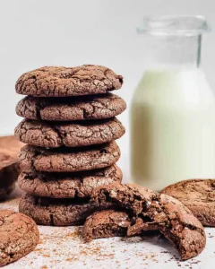 A stack of double chocolate chip cookies, one with a bite out of it, and a jug of milk.