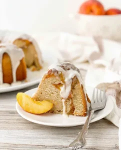 Slice of peach-glazed cake on a white plate with a fork, peach wedges on the side.