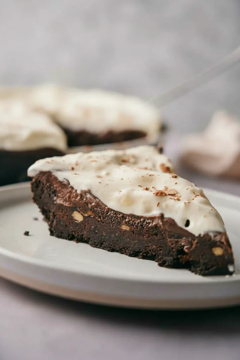 Mississippi-mud-pie-19-682x1024.jpg A slice of rich chocolate cake with white frosting and chopped nuts on a white plate.
