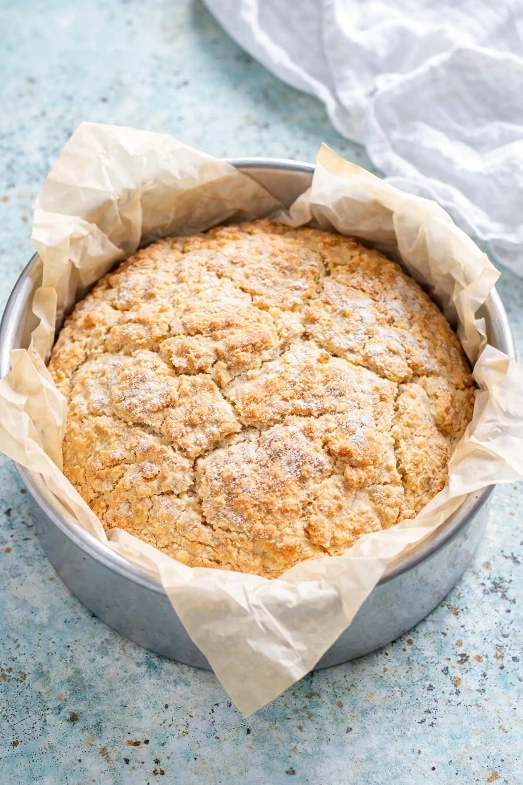 round loaf with a crackled crust in parchment-lined pan on a pale blue surface