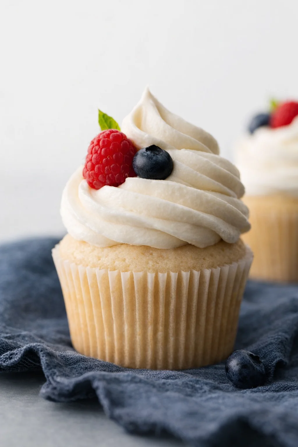 A vanilla cupcake with white frosting and a raspberry and blueberry on top.
