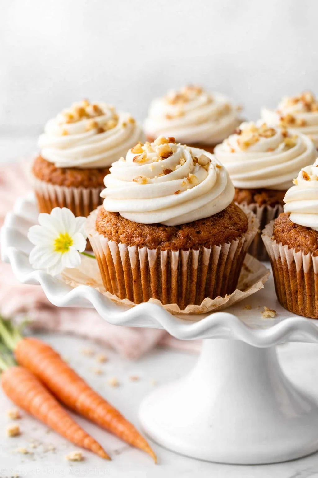 Carrot cupcakes with white cream cheese frosting on a white pedestal cake stand.