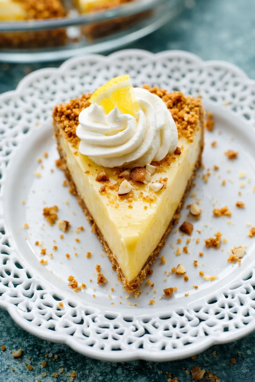 slice of lemon cheesecake on a decorative white plate with whipped cream and lemon zest