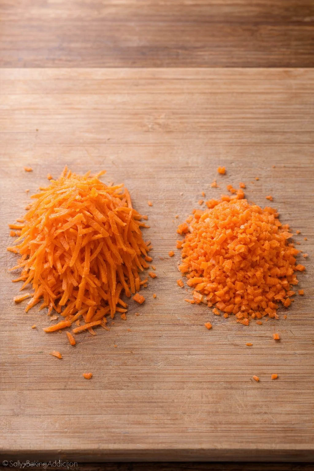 Two piles of carrot shreds on a wooden cutting board, left shredded, right shredded and chopped