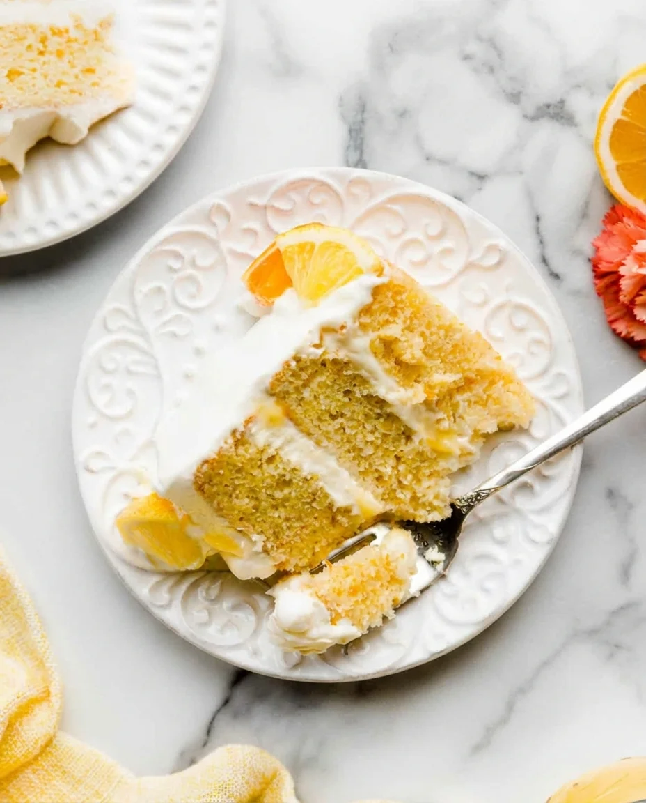 slice of citrus cake with orange garnish and whipped cream on a white decorative plate