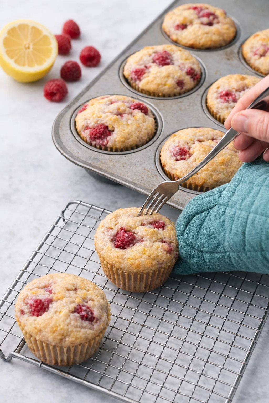 Fork loosening muffin edges while an oven mitt lifts one onto a cooling wire rack.