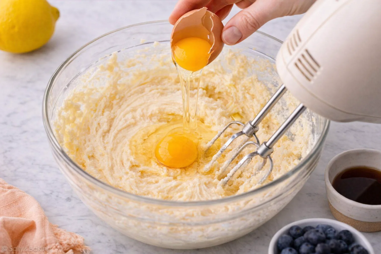 Mixer bowl with batter as oil is poured and eggs are added one at a time.
