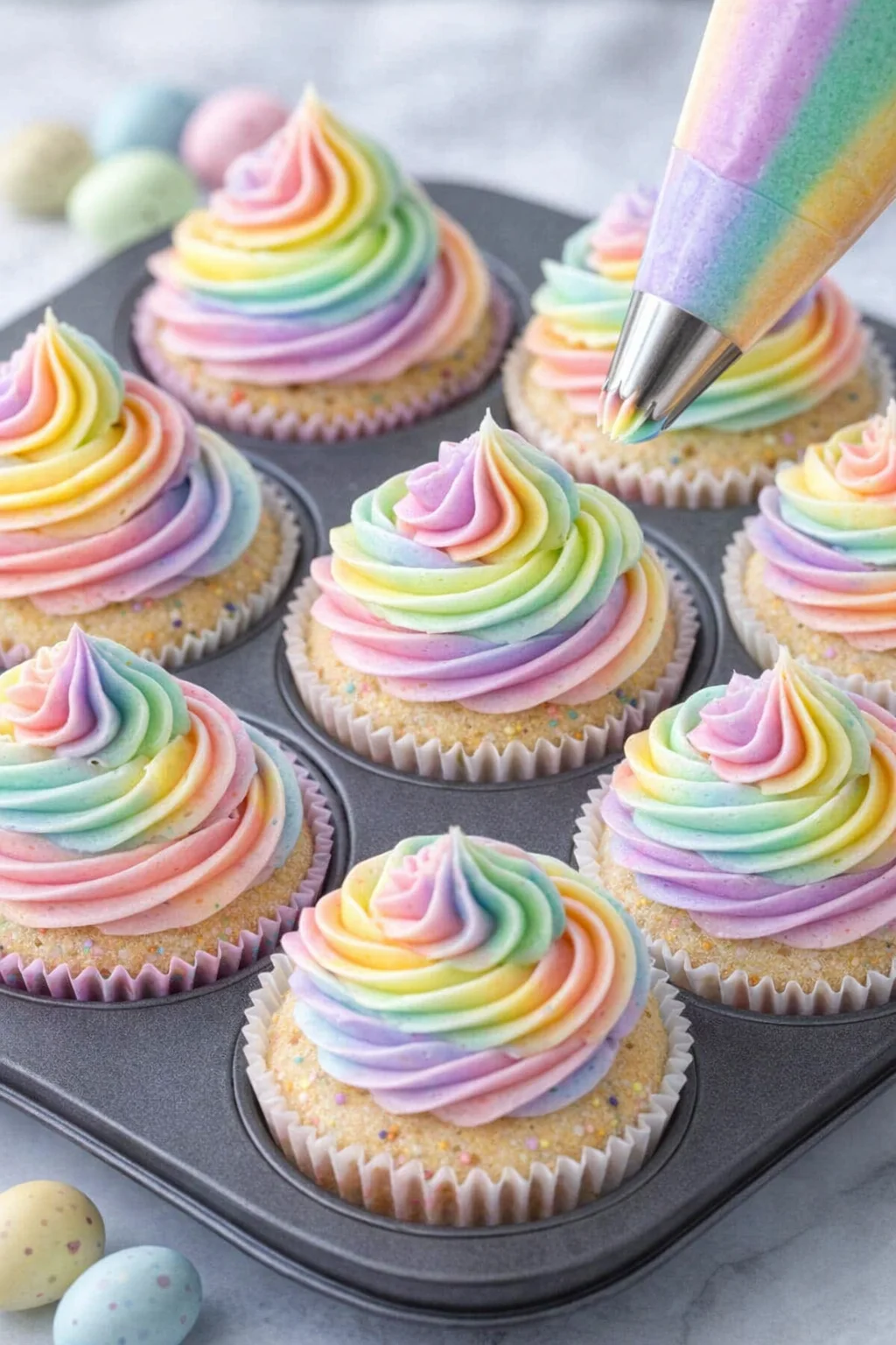 Multiple cupcakes topped with multicolored rainbow buttercream swirls piped from a single bag.