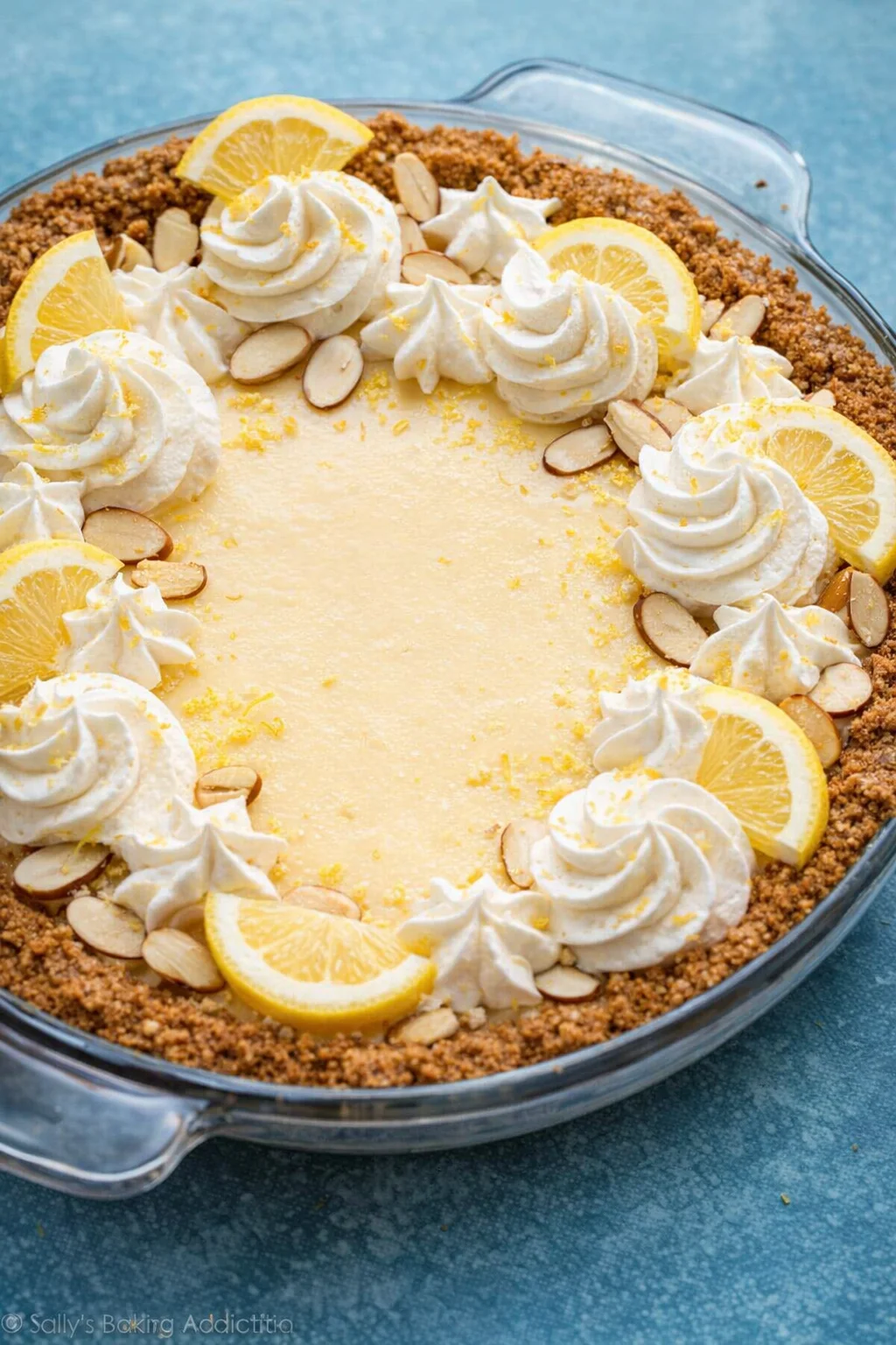 Finished lemon pie topped with whipped cream, lemon zest, and scattered toasted almonds.