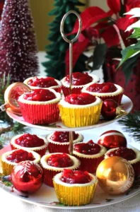 2-Tiered plate with cheesecake cupcakes in red and gold foil liners, and glass Christmas tree balls.