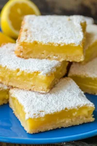 Lemon bars with powdered sugar topping stacked on a blue plate