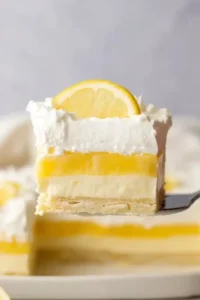 Slice of lemon lush dessert with creamy layers and whipped topping on white plate