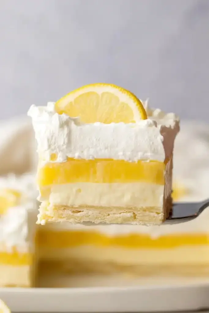 Slice of lemon lush dessert with creamy layers and whipped topping on white plate