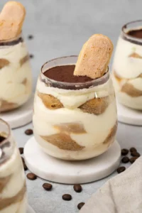 4 Mini tiramisu cups in a glass on a table top.