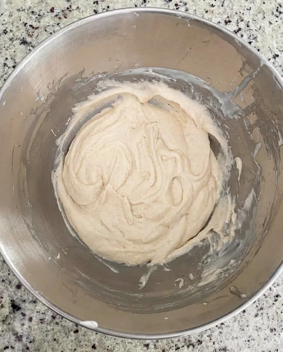 Overhead view of smooth, ivory batter swirled in a stainless steel mixing bowl.