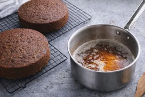 Two layers of moist carrot cake cooling on a wire rack with caramel sauce in a saucepan