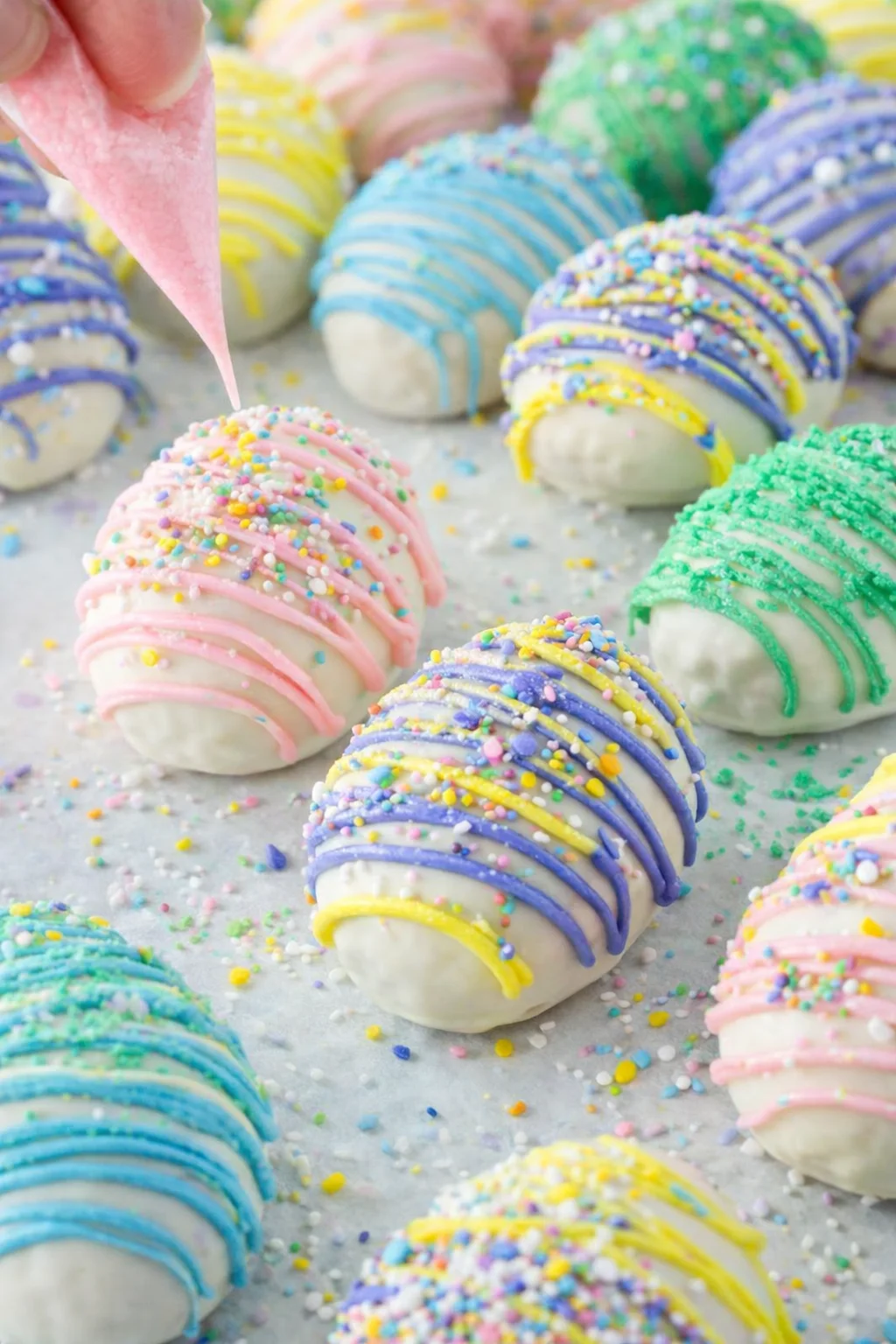 Piping pastel drizzle over coated eggs, then pressing sprinkles on wet coating to set.