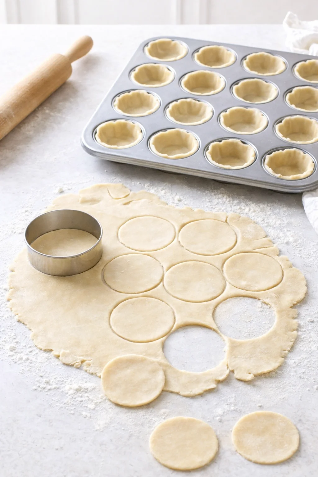 Thin dough circles cut and pressed into muffin tin wells forming tart shells.
