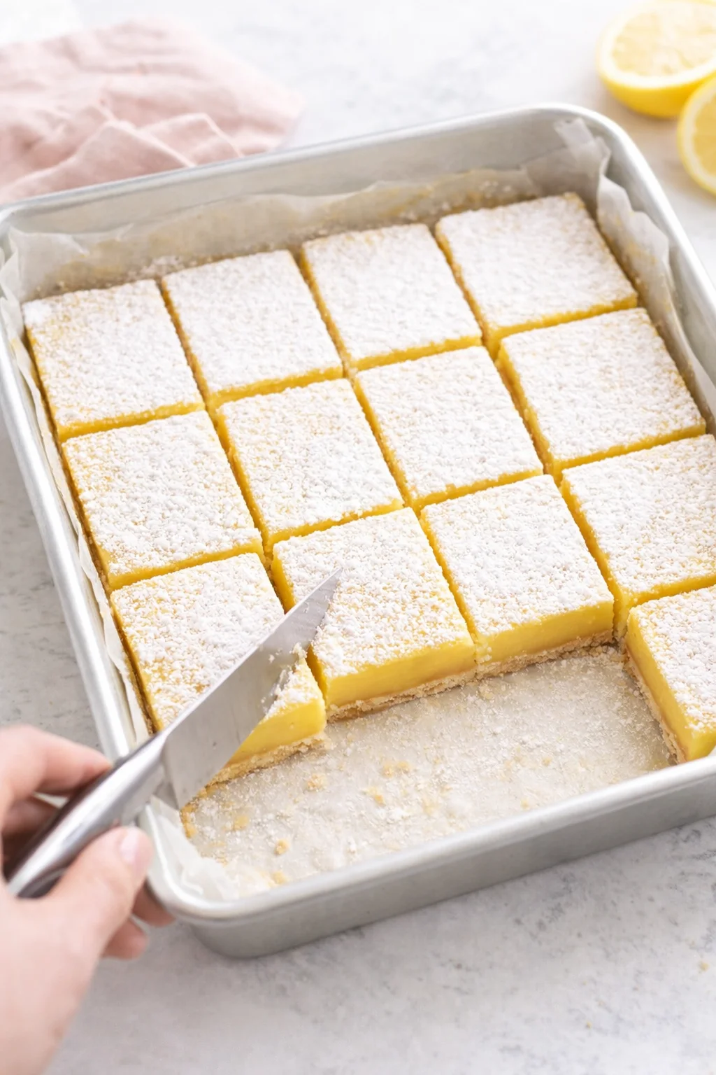 Lemon bars dusted with powdered sugar, neatly cut into squares on parchment.
