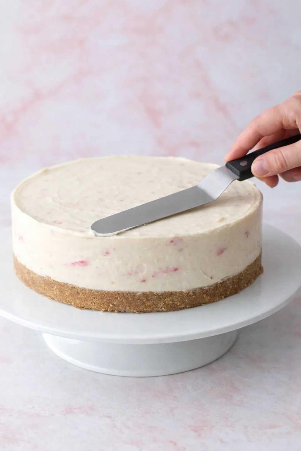 Cheesecake filling spread and smoothed over chilled crust, springform ring released and sides smoothed