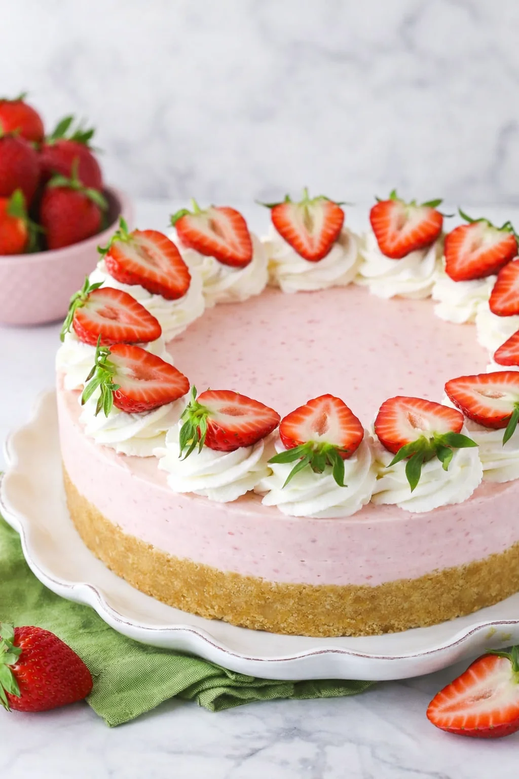 Cheesecake on serving plate decorated with piped whipped cream swirls and sliced strawberries.