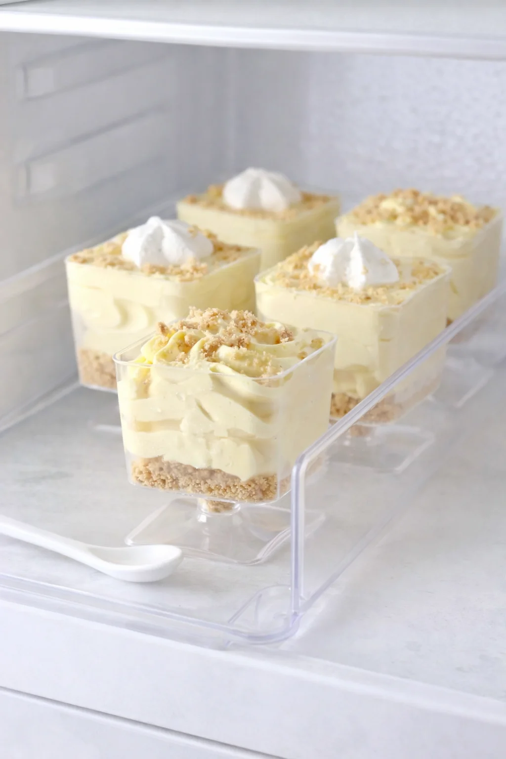 Clear cups arranged on tray inside fridge chilling to set the lemon cheesecake mousse.