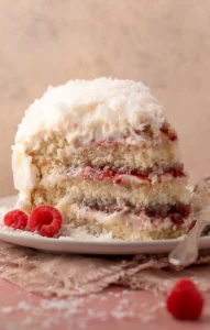 Slice of coconut cake on a white plate with a fork on the side.
