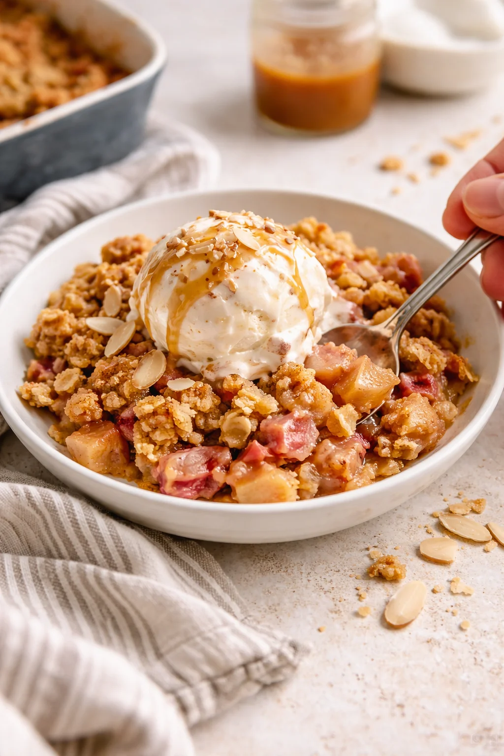 bowl of warm apple crumble topped with vanilla ice cream, caramel drizzle, and almond slivers