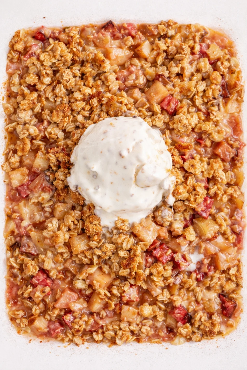 Square baking dish of apple crumble with oats and a scoop of vanilla ice cream on top