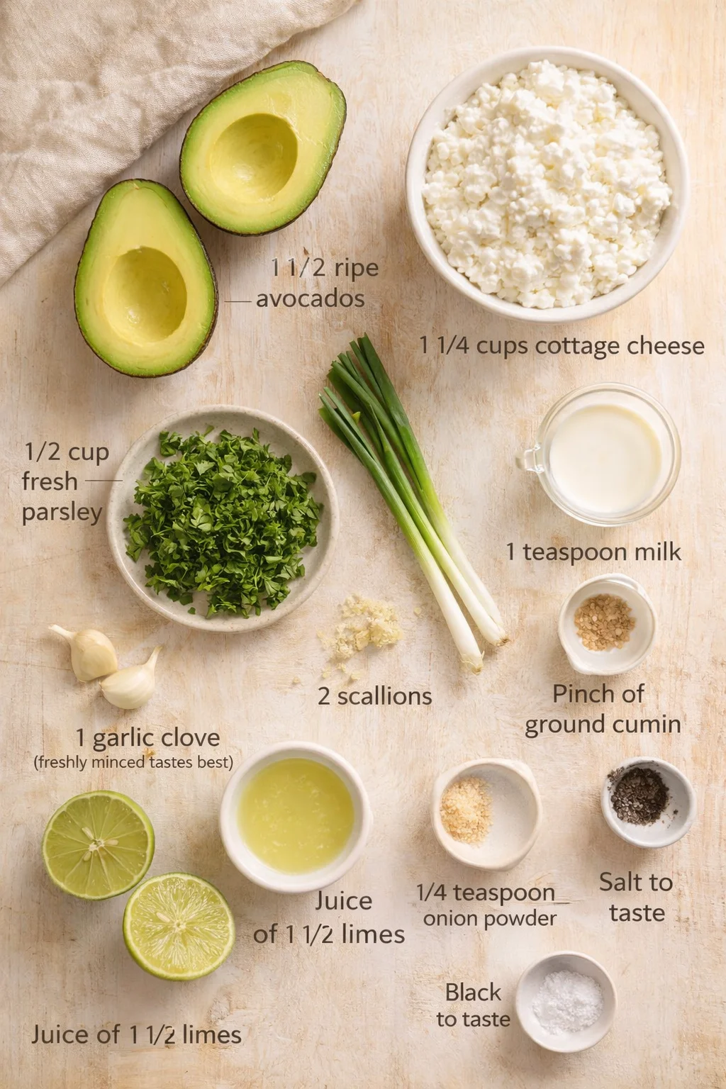 Overhead shot of avocado halves, cottage cheese, herbs, limes, and other ingredients on a wooden board