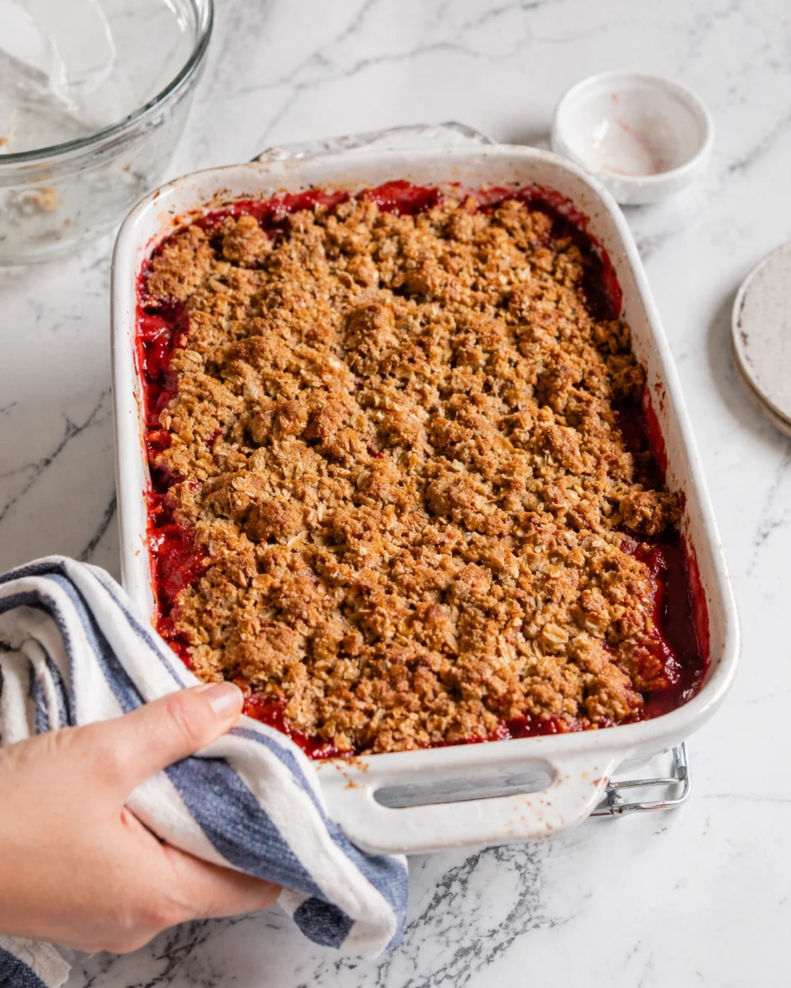 A white ceramic baking dish filled with berry crumble, golden crumb topping, on a marble counter.