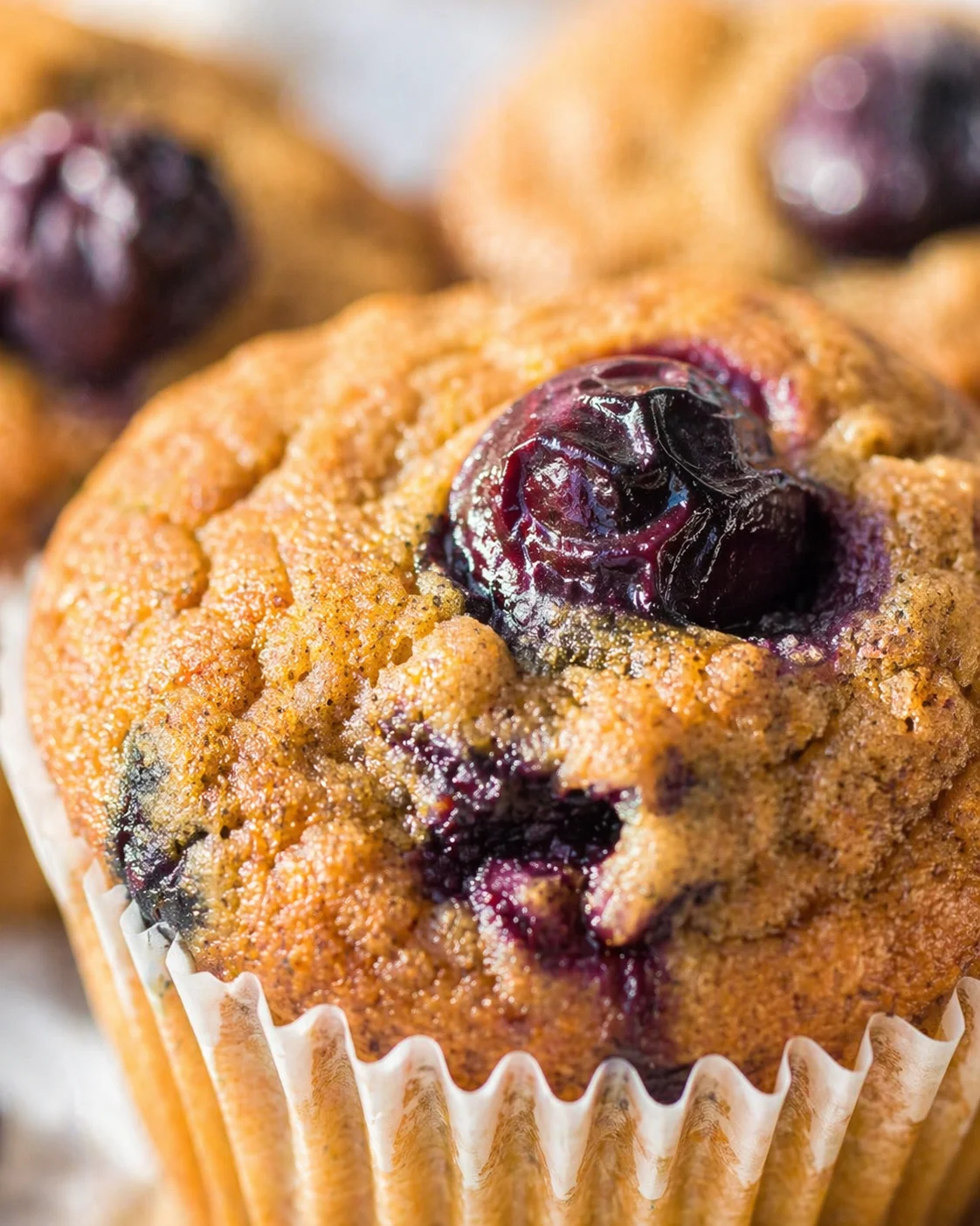 Close-up of golden blueberry muffins with crumb topping and purple filling in paper liners.