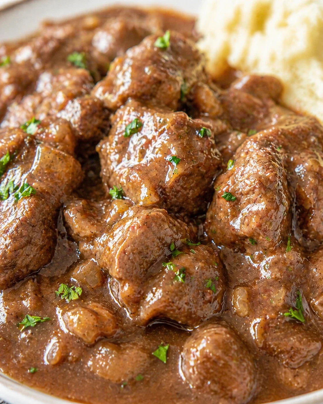 Close-up of beef chunks in glossy brown gravy with parsley garnish
