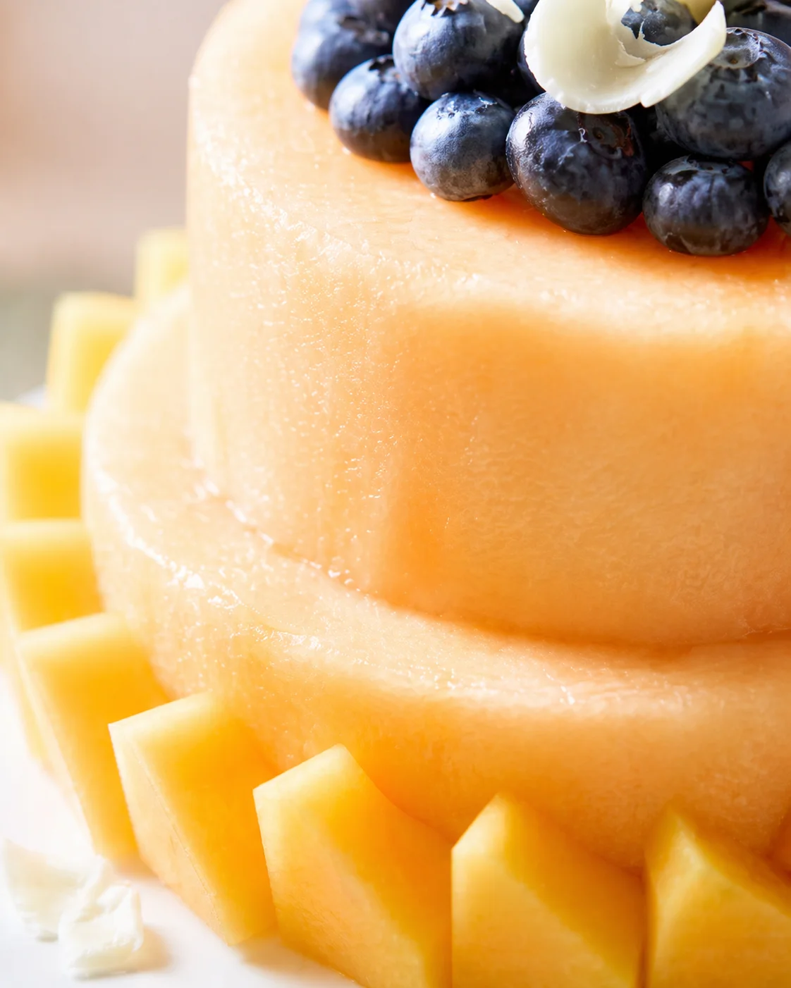 close-up of cantaloupe-based cake topped with blueberries and a white chocolate curl.