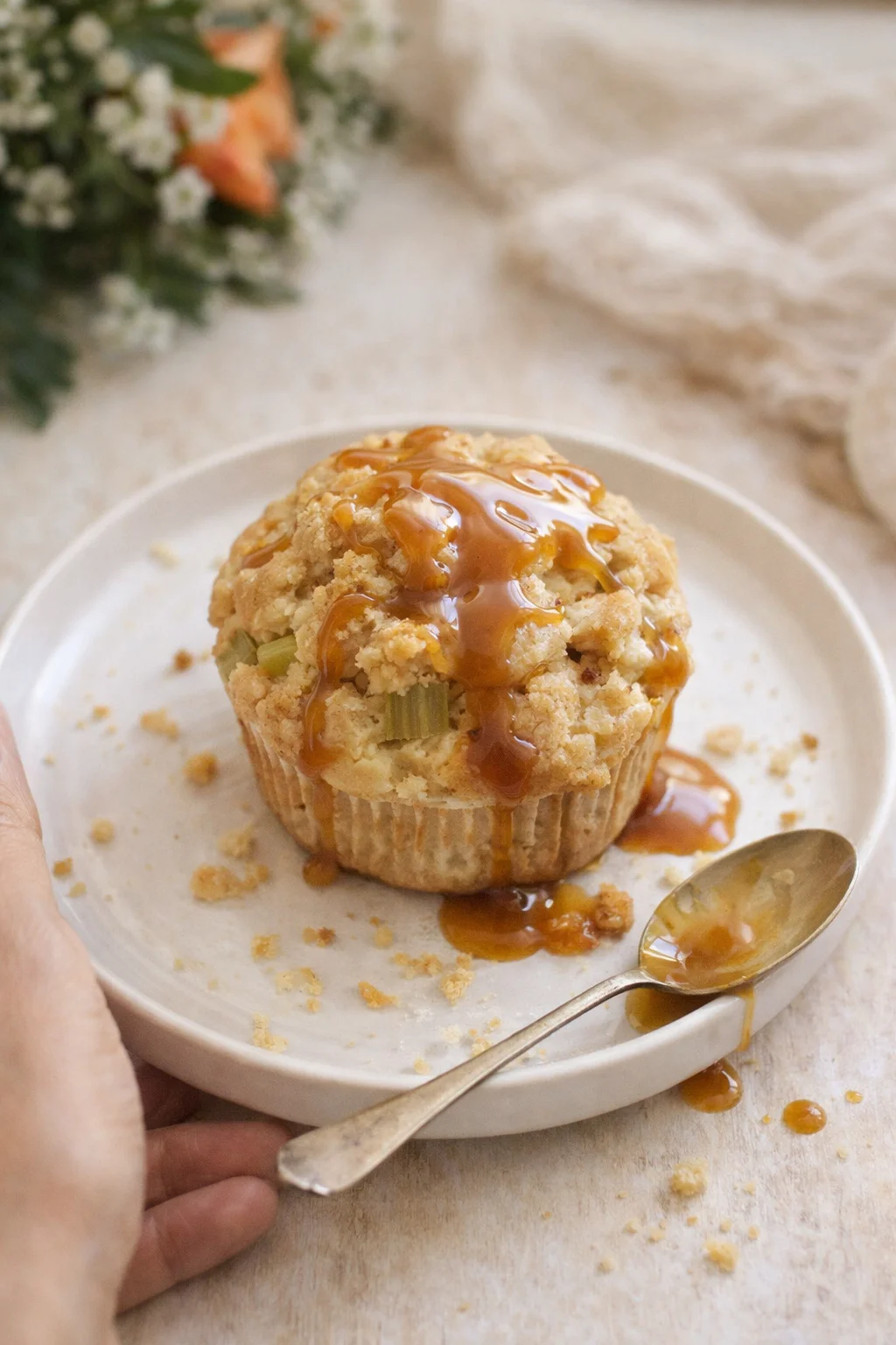 caramel-drizzled crumble muffin on a white plate with a spoon