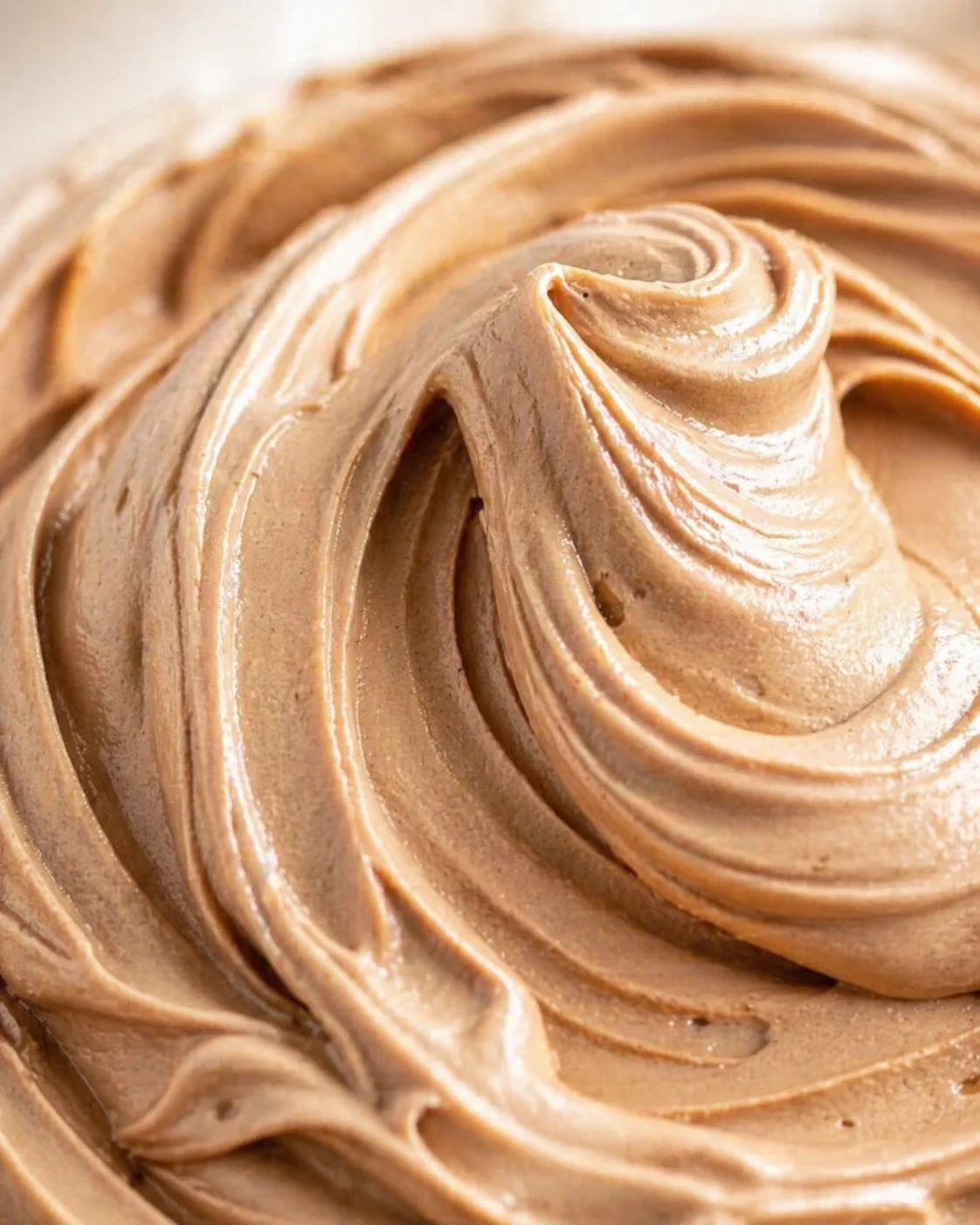 Close-up of silky, glossy chocolate buttercream swirls on a smooth surface
