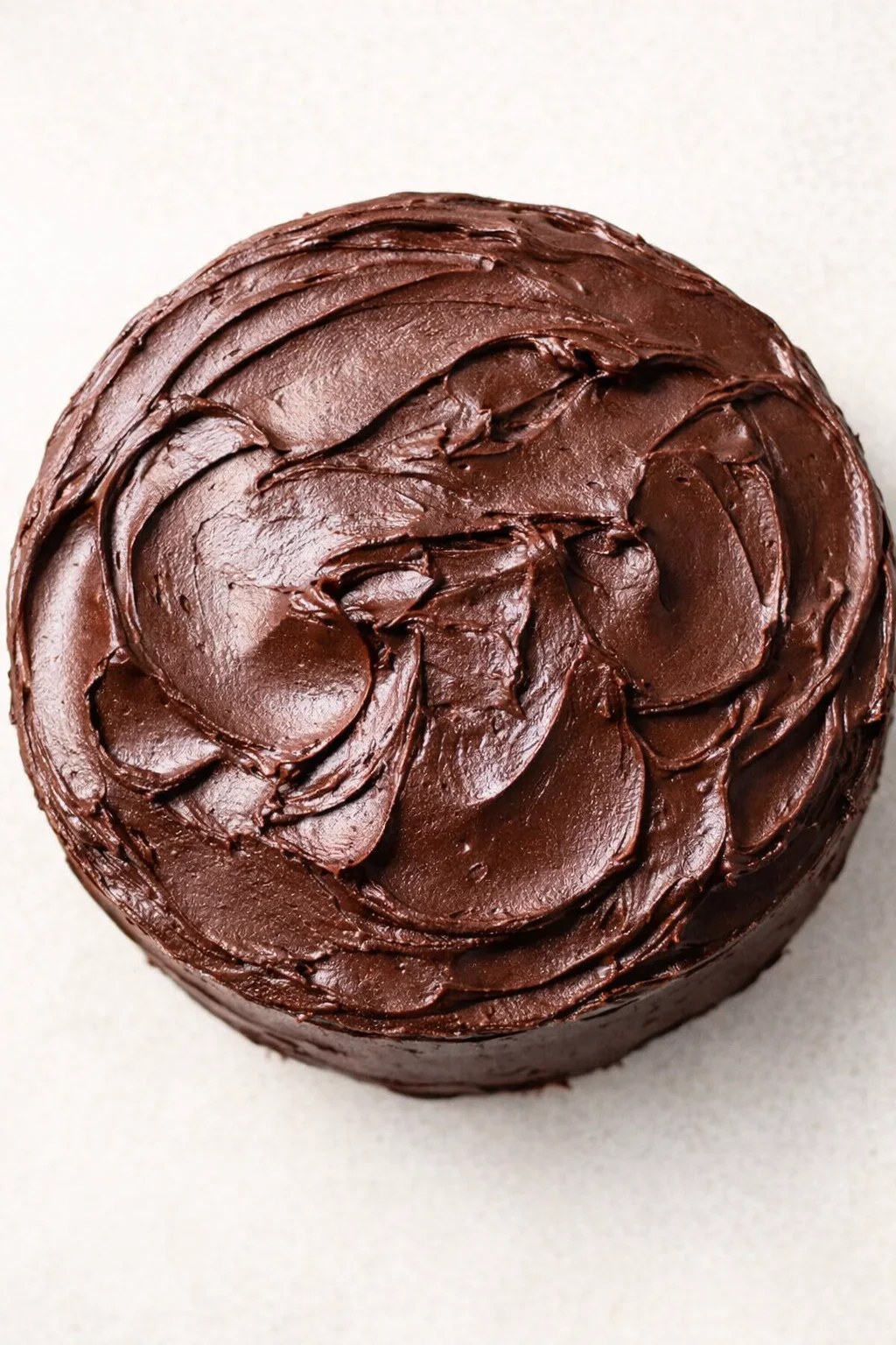 Top-down view of a round chocolate cake with rich swirled frosting on a light background.