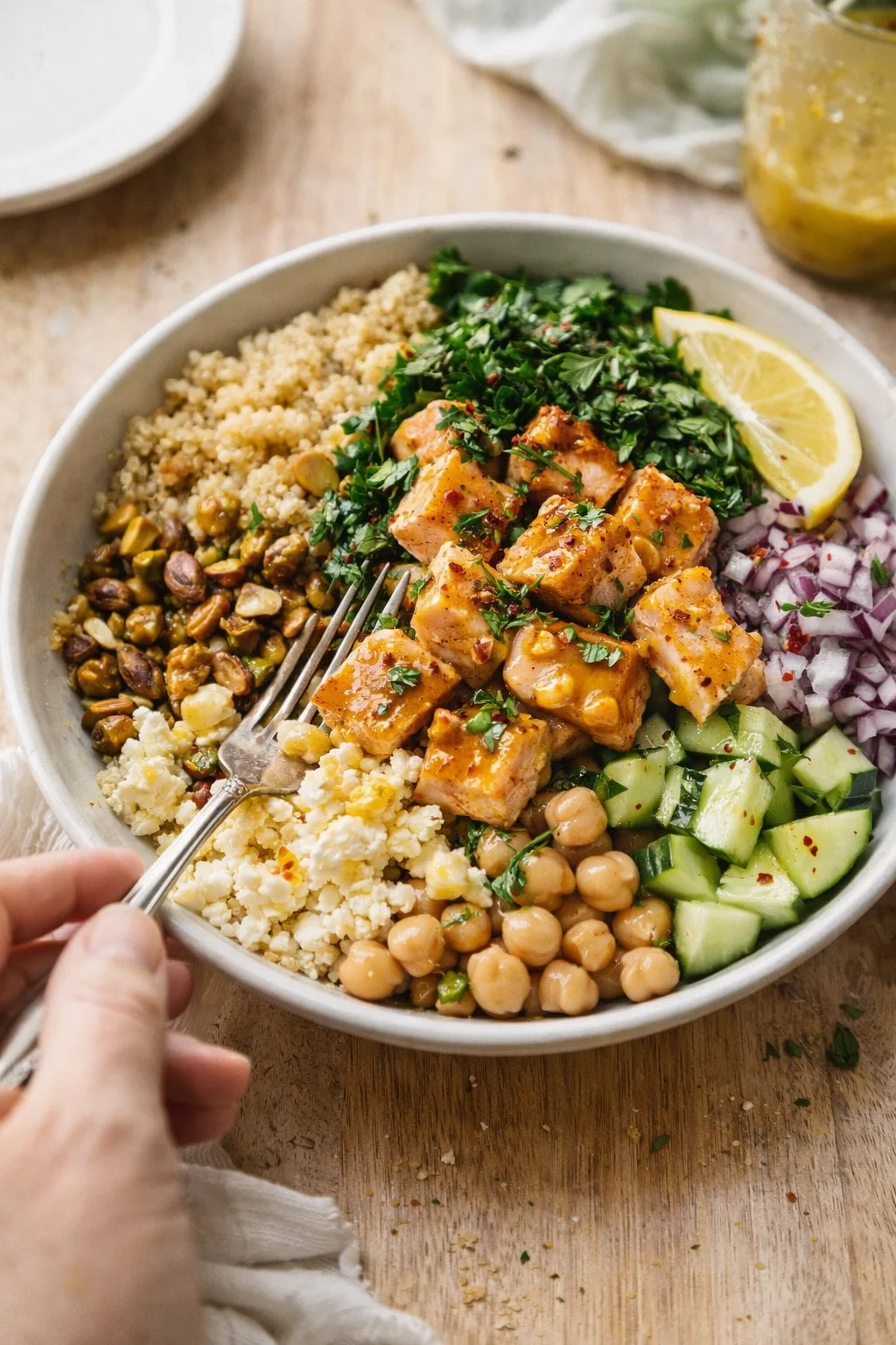 A colorful Buddha bowl with orange-glazed cubes, chickpeas, cucumber, red onion, quinoa, herbs, and a lemon wedge.