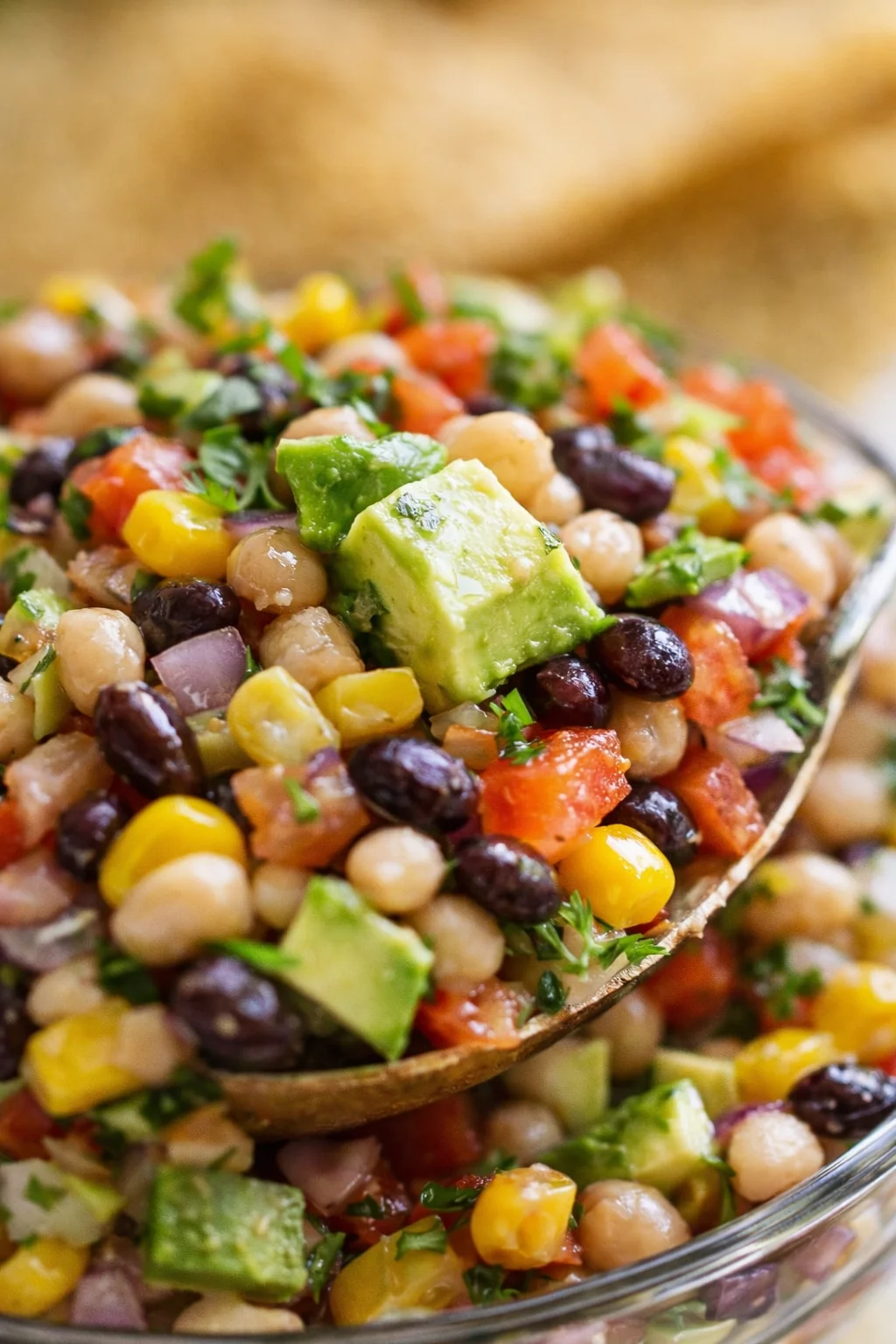 close-up of a colorful chickpea-avocado salad with corn, tomatoes, red onion, and cilantro