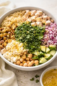Colorful grain bowl with quinoa, chickpeas, diced tofu, feta, cucumber, red onion, and herbs.