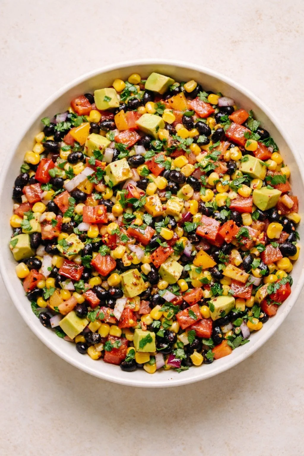 white bowl of colorful corn, black beans, avocado, red pepper, onion, and cilantro salad