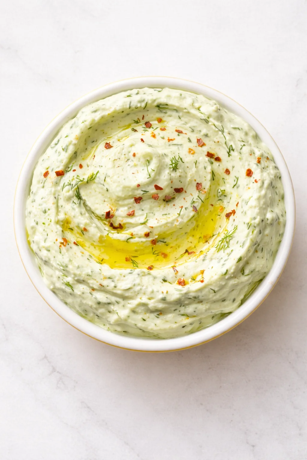 Creamy dill yogurt dip swirled in a white bowl with oil and red pepper flakes