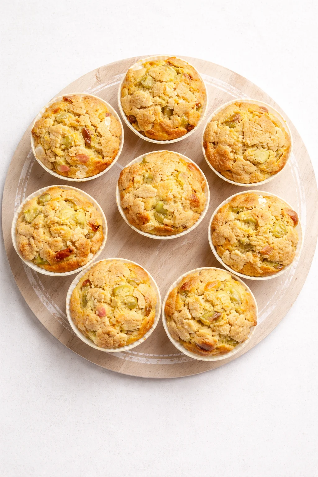 Top-down view of nine crumb-topped apple muffins on a round wooden board.