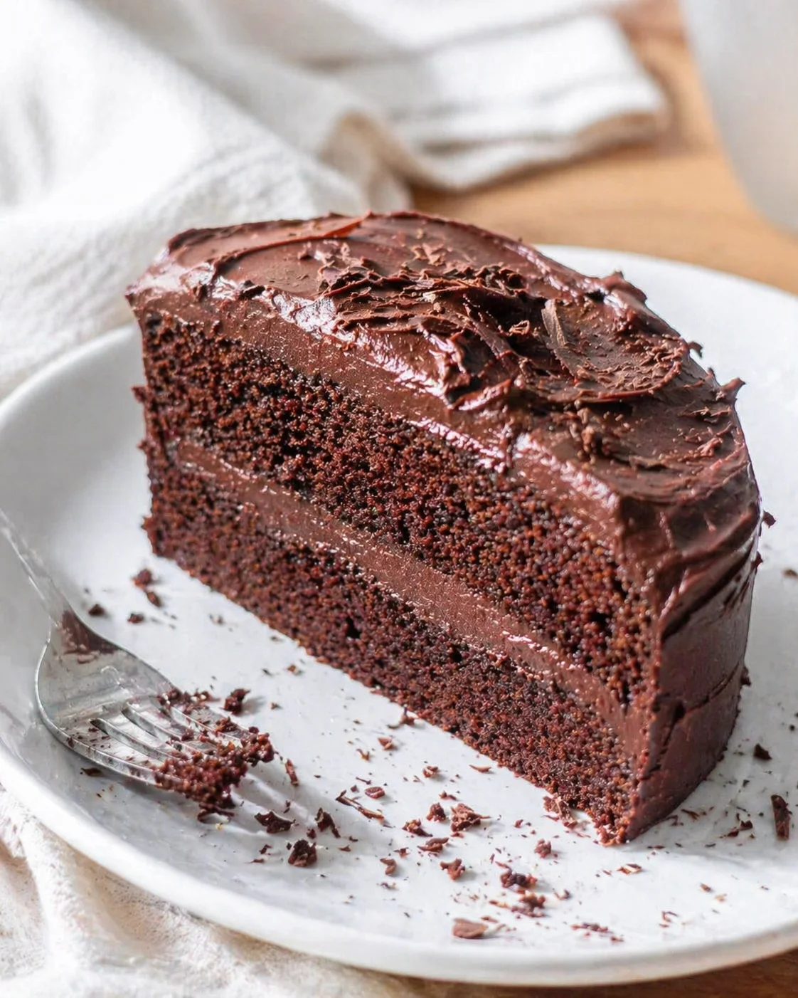 slice of glossy chocolate cake on a white plate with shavings and crumbs