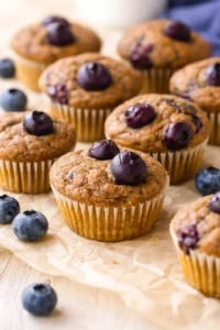 Golden blueberry muffins on parchment paper with blueberries scattered nearby
