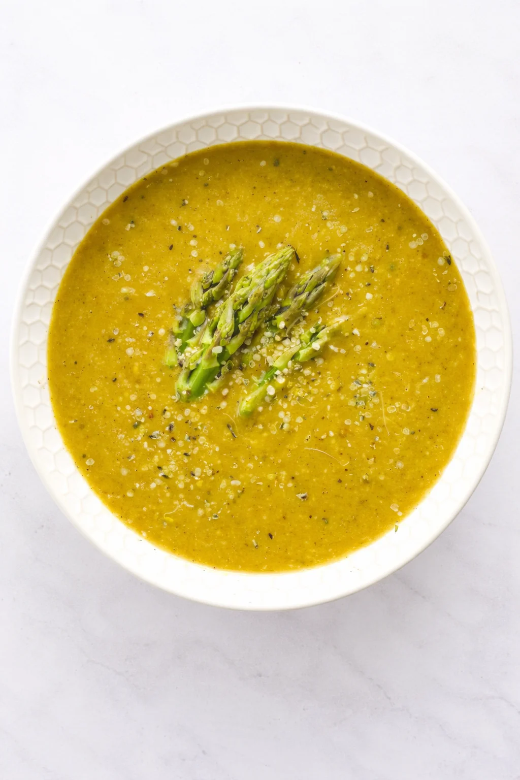 Creamy golden soup in a white honeycomb-edged bowl, topped with asparagus spears.