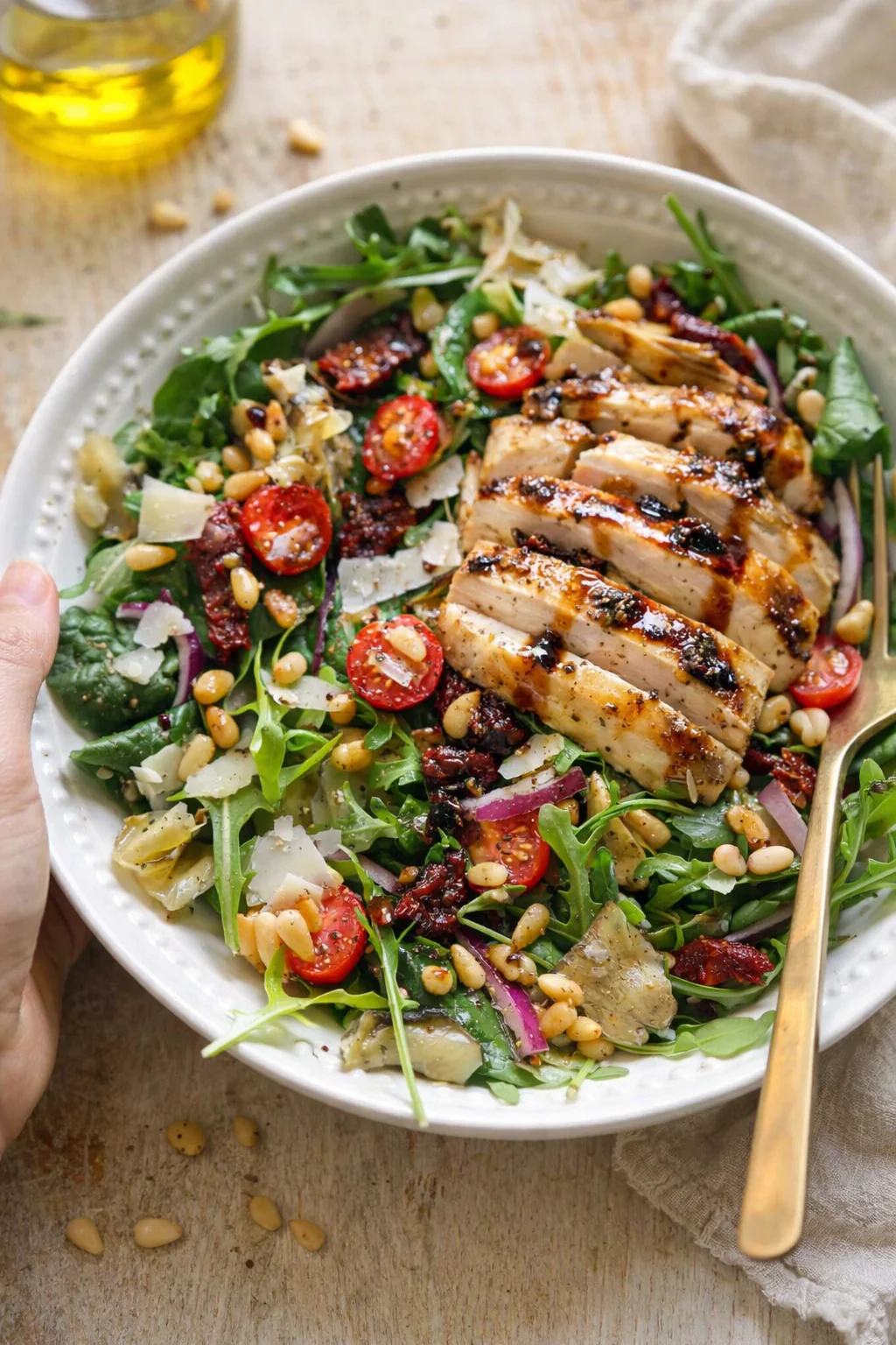Plated grilled chicken salad with greens, cherry tomatoes, parmesan, and pine nuts.