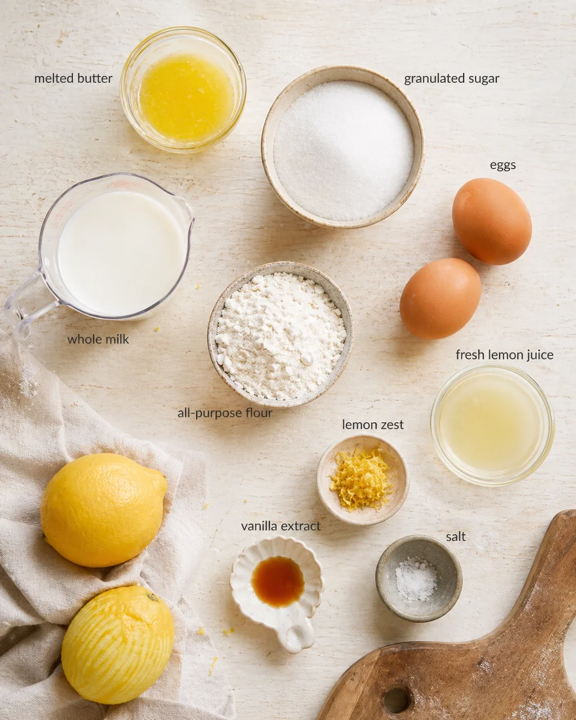 Top-down view of lemon cake ingredients labeled on a light wooden surface.