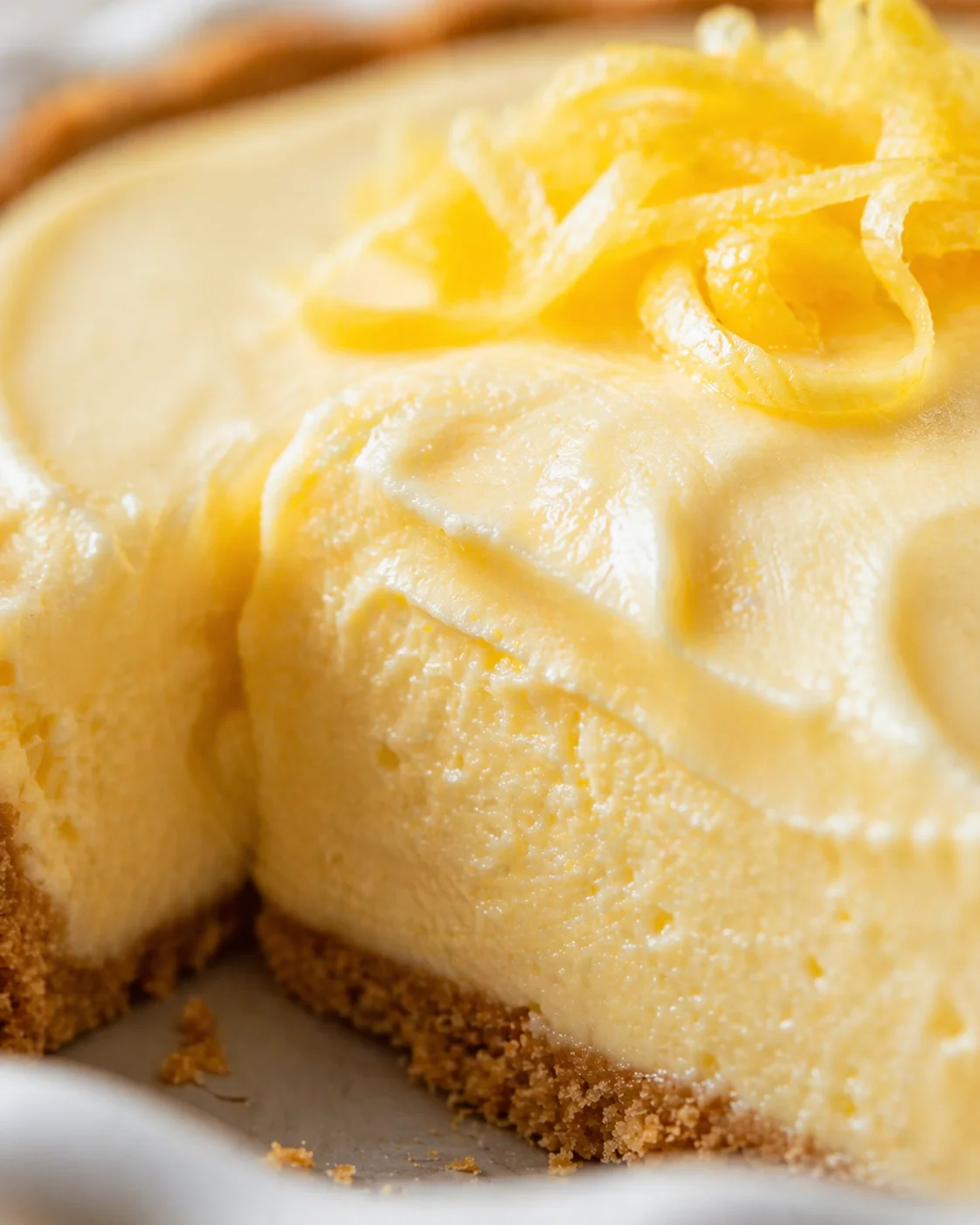 Close-up of lemon cheesecake slice with lemon zest curls and crumb crust.